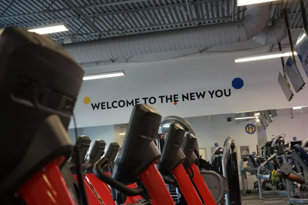 A row of red treadmills. Welcome to the new you is on the upper part of a wall.