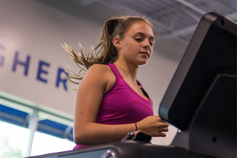 A young woman looking at the screen of a treadmill while running.