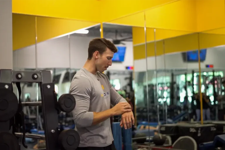 A man standing next to a weight rack, looking at a wristwatch.
