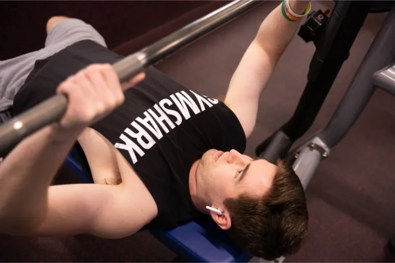 A man in a black tank top holds a weight bar while lying on a flat bench.