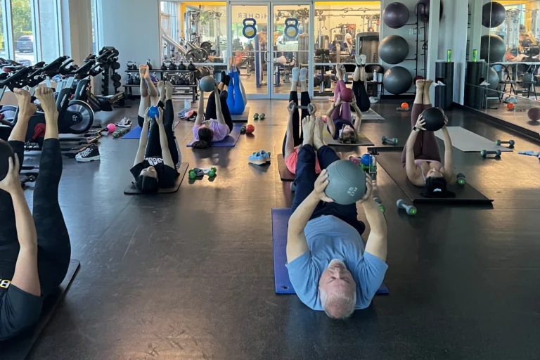 A group of nine people doing the leg raises with a medicine ball exercise at a gym.
