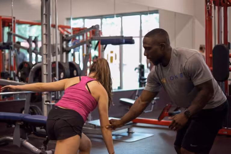 Male fitness instructor helping a female gym goer exercise at a fitness center.