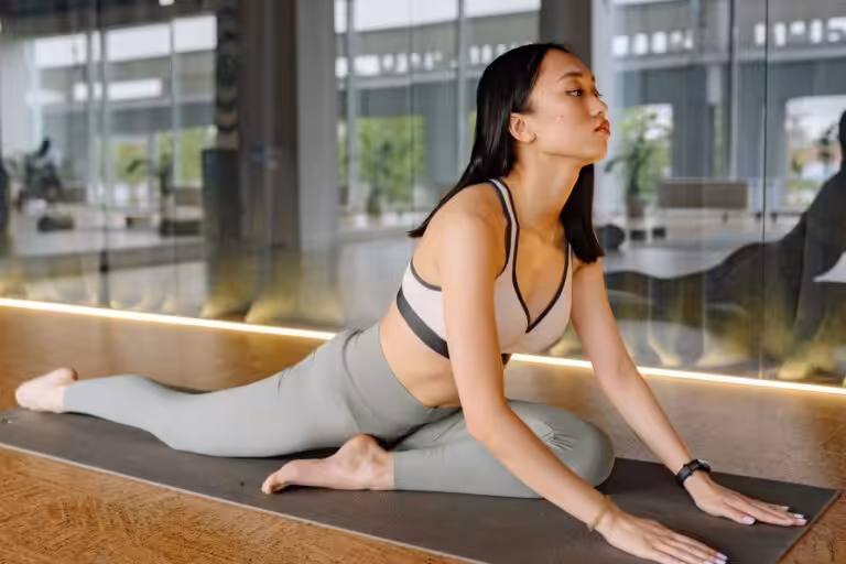 A woman performing the pigeon pose on a yoga mat.