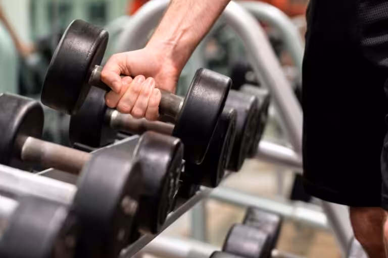 A man's hand picking up a dumbbell.