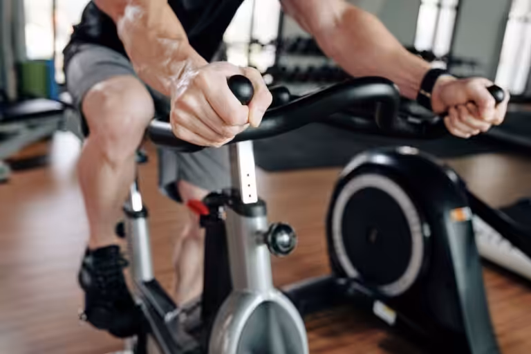 Man's hands holding the handles of an exercise bike.