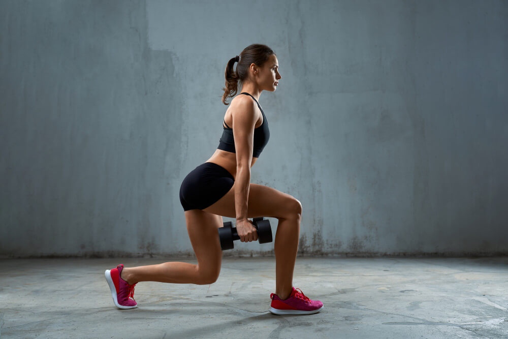 A woman doing hamstring march exercise with dumbbells indoors.