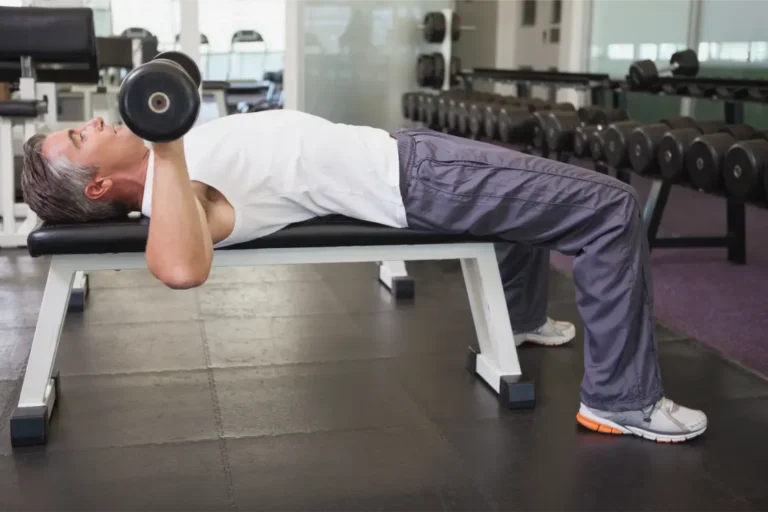 A man lying on a flat bench doing dumbbel bench press exercise at a gym.