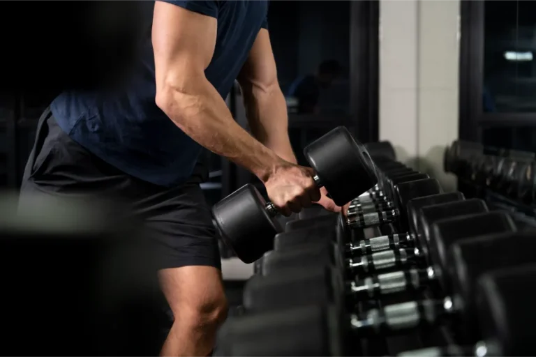 A man's arm picking up a dumbbell of the weight rack.