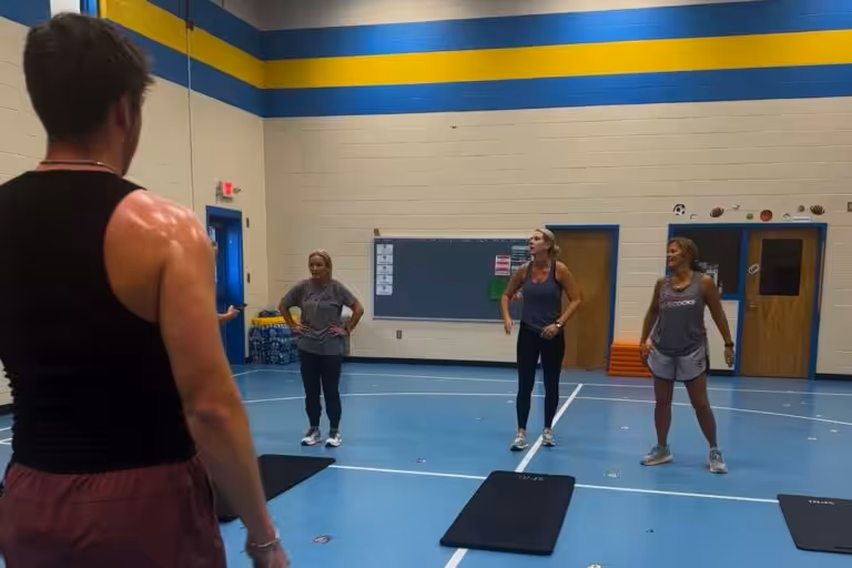 Man in the foreground is facing three women in the background who stand in front of their yoga mats.