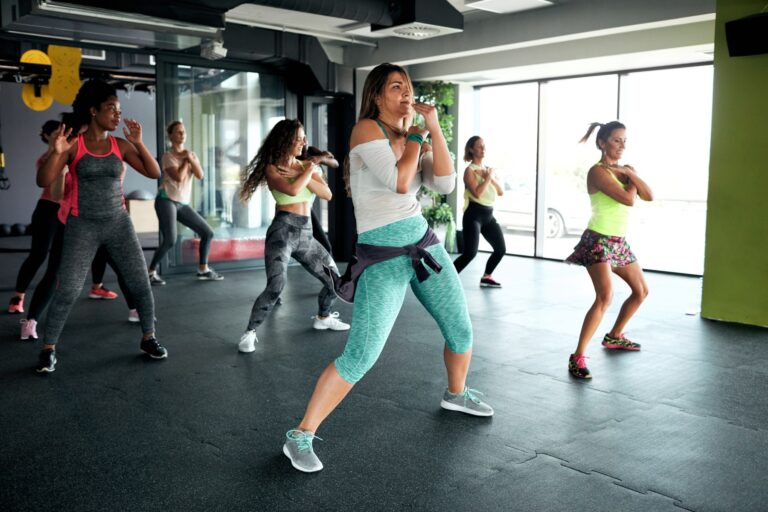 Seven women doing a Zumba class at a fitness center with a padded floor.