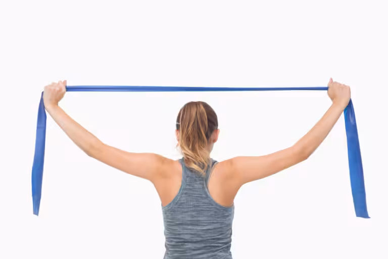 A woman in a gray workout tank holds a blue resistance band with both hands, extending it behind their head.
