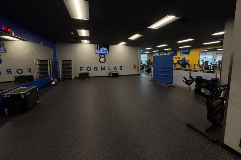 Empty gym with black floors, mirrored wall, weights, exercise bikes, and "8 FORMLAB" text on a white wall.