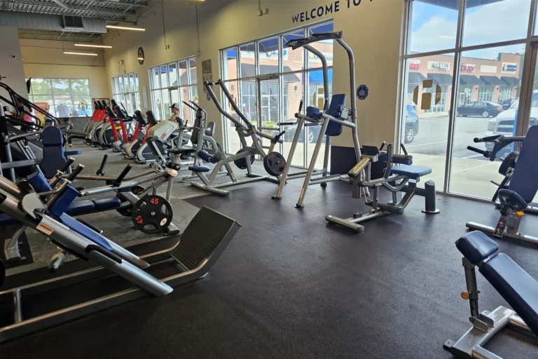 Gym with leg press, cable machines, and selectorized weight equipment in front of large windows.