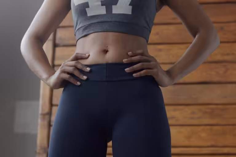 Torso of a woman in a gray crop top and dark leggings with hands on hips.