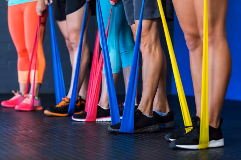 Legs of four people on the black floor. Each person stands on a resistance band with one foot.
