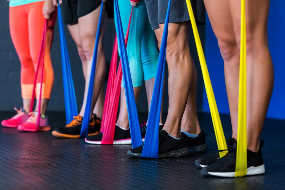 Legs of four people on the black floor. Each person stands on a resistance band with one foot.