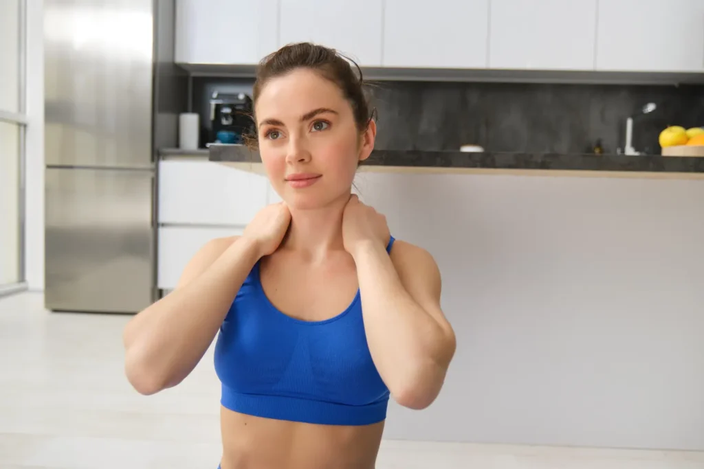 Woman in a blue sports bra stretches her neck, looking ahead in a modern kitchen.