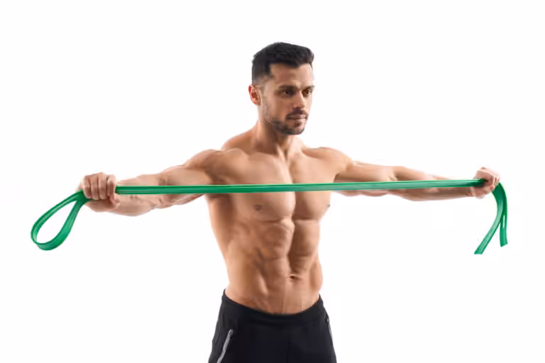 A muscular man in black shorts pulls a green resistance band horizontally across his chest.