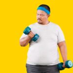 An obese man in a white t-shirt and blue headband lifts a small dumbbell. Yellow background.