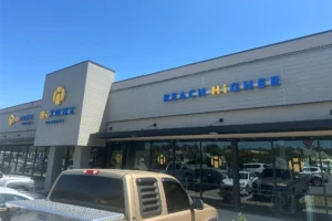 A store with the signs "HiTONE Fitness" and "REACH HIGHER" in blue lettering. A truck is parked in front.