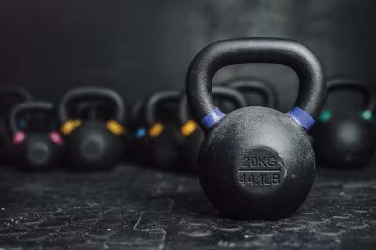 Black 20kg 44LB kettlebell with blue stripe on textured rubber floor with colorful kettlebells blurred in background.