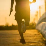 Silhouette of person running on wooden boardwalk at golden hour sunset with bridge and buildings in background.