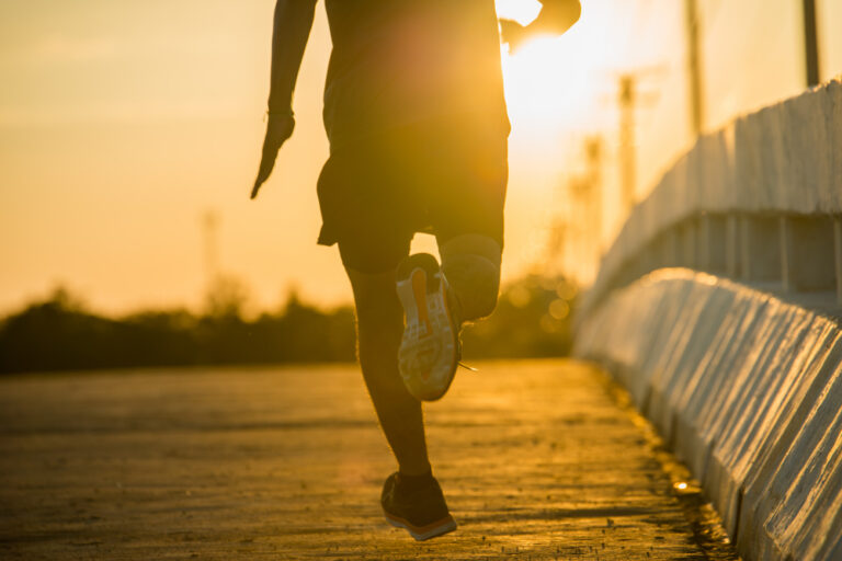 Silhouette of person running on wooden boardwalk at golden hour sunset with bridge and buildings in background.
