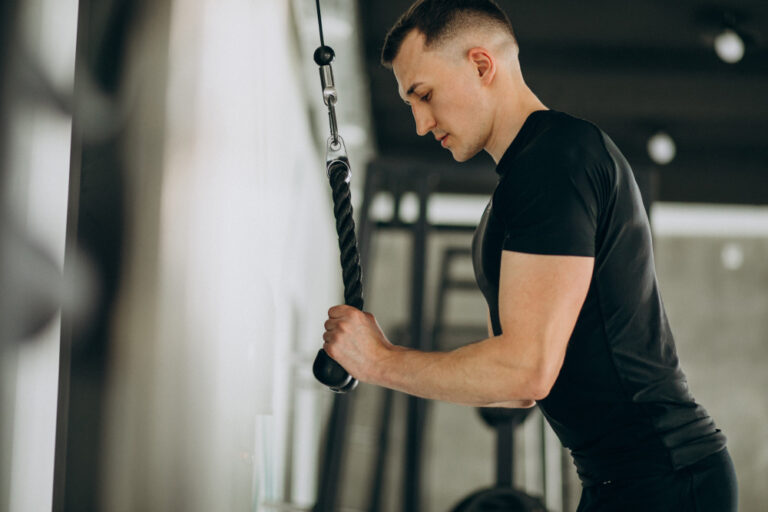 A man in a black shirt does triceps pushdowns on a cable machine.