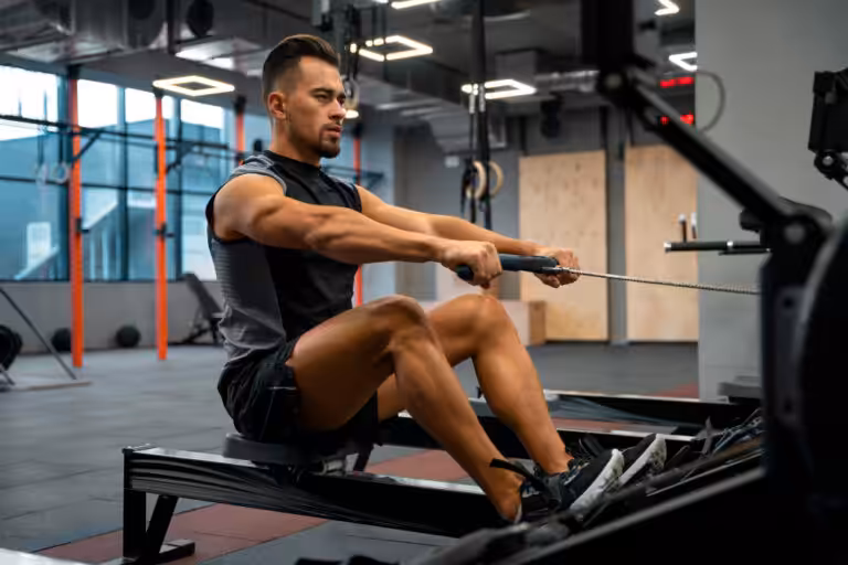 Muscular man in black tank top performing seated cable row exercise on black gym equipment in modern fitness center.
