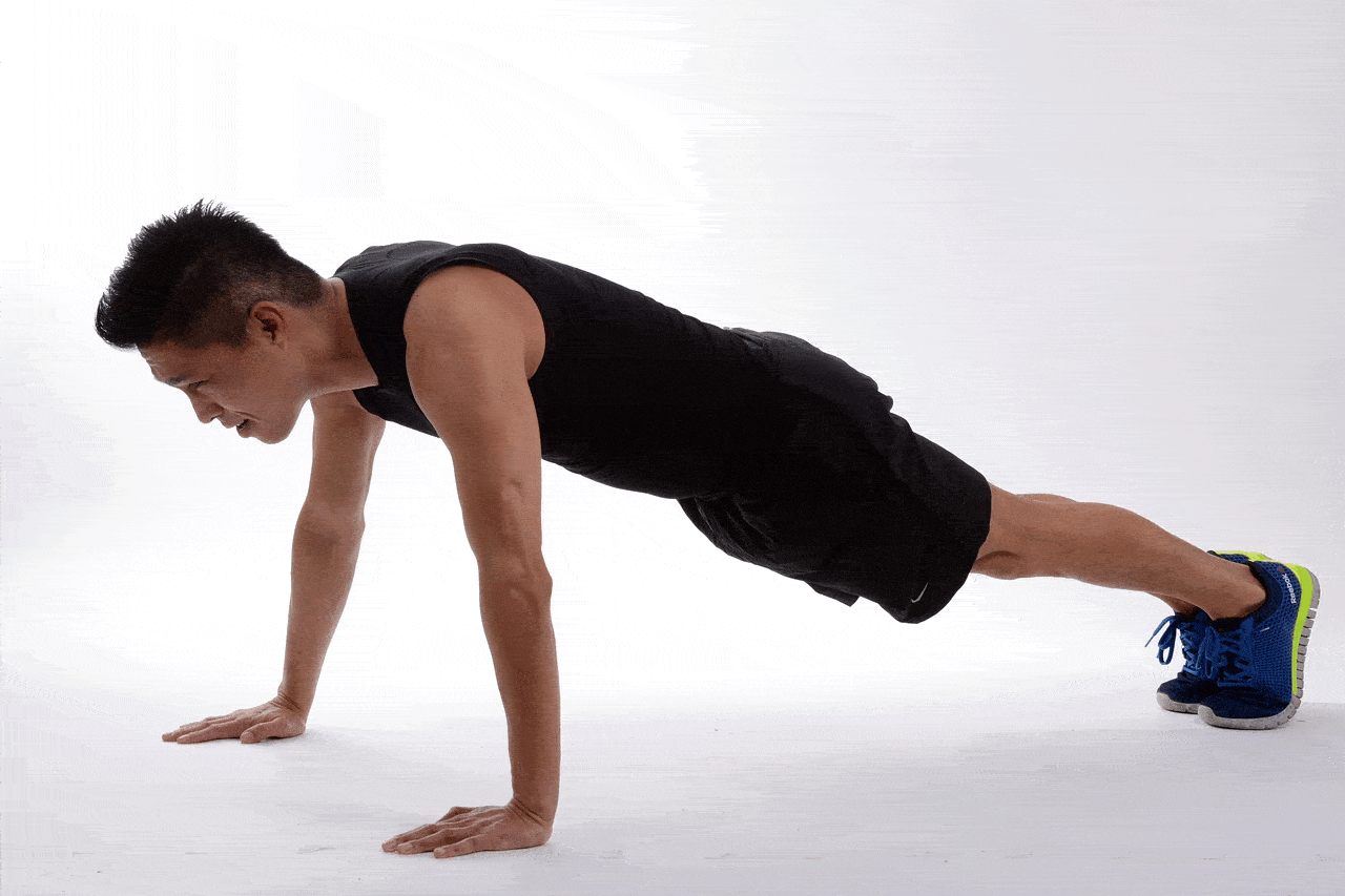 A man in black sportswear and blue sports shoes does push-ups against a white background.