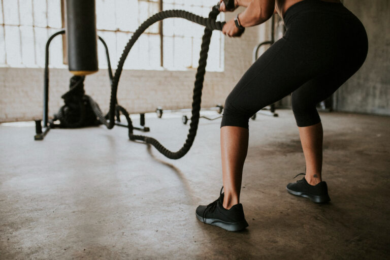 Woman in black capri leggings using battle ropes in industrial gym with concrete floors and metal beams.