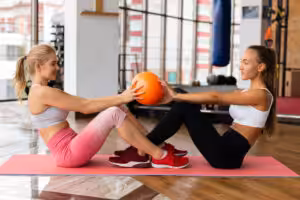 Two women exercising with yoga mat and medicine ball.