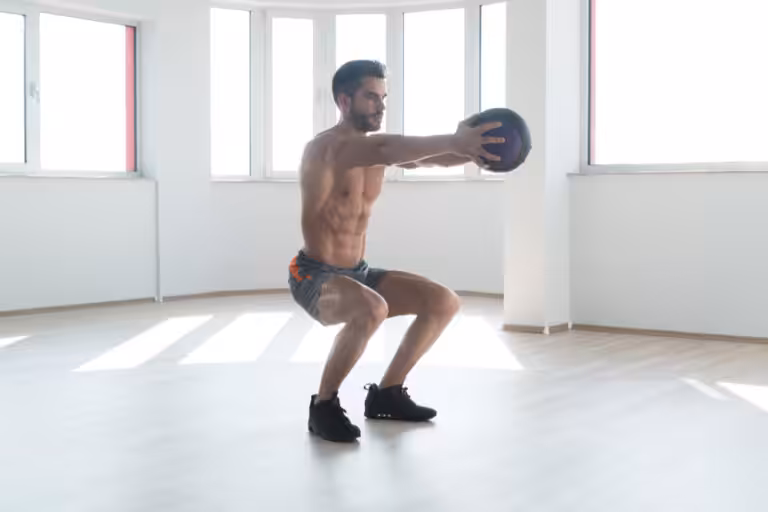Man doing squats with medicine ball indoors.