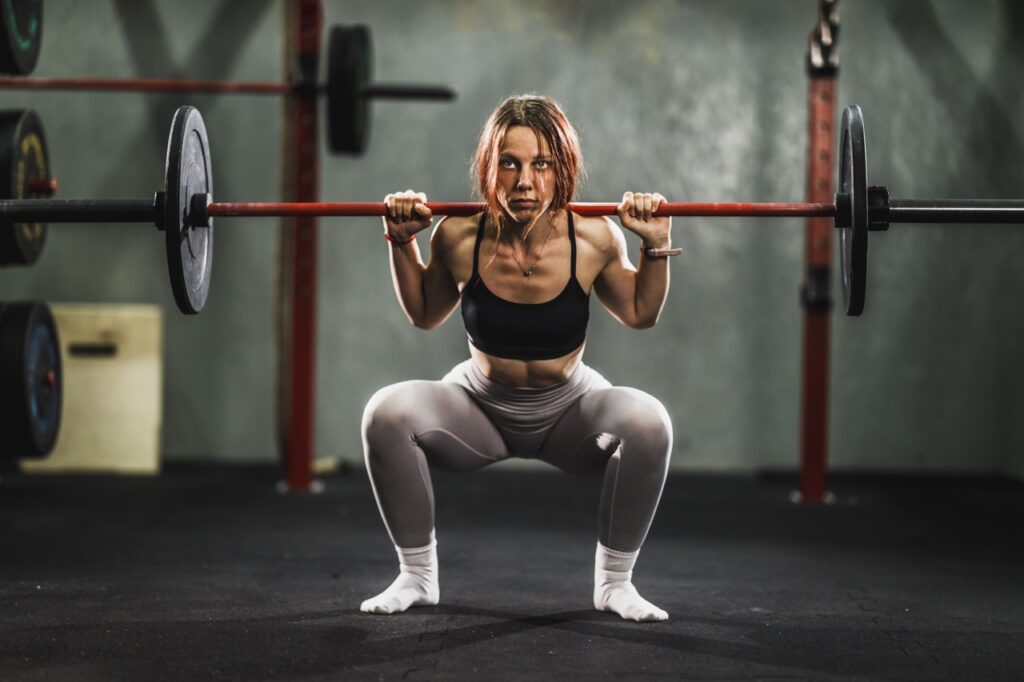 Woman performing barbell back squat in gym