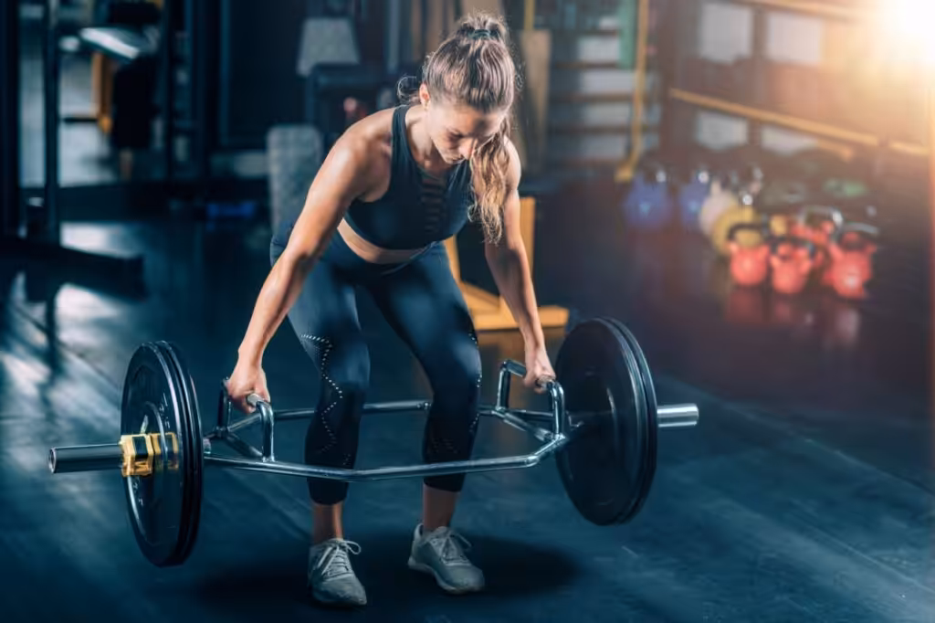 Woman performing trap bar deadlift in gym.