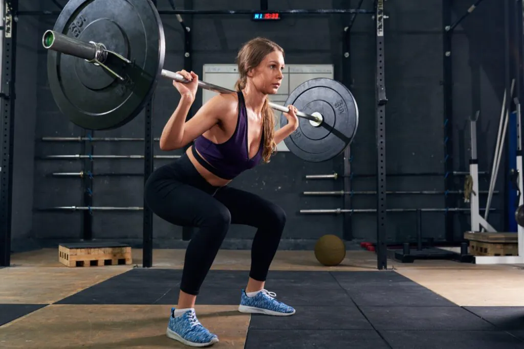 Woman performing barbell back squat in gym