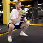 Man performing kettlebell goblet squat in gym.