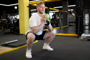 Man performing kettlebell goblet squat in gym.