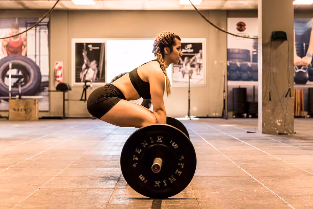 A woman with braided hair doing a deadlift at a gym.